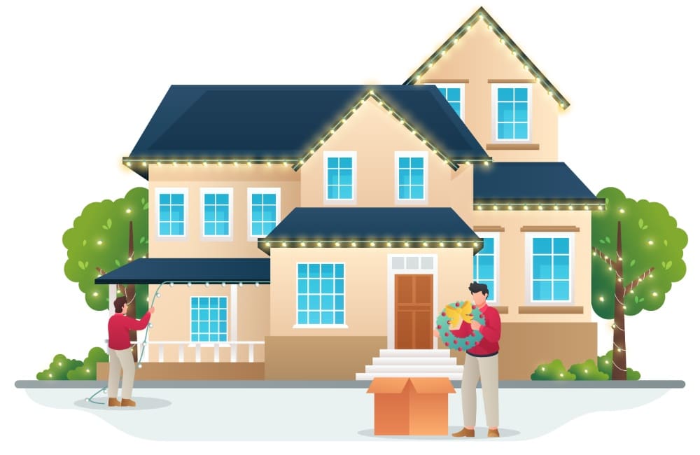 A two-story house is being decorated for Christmas with lights along the roofline. One person holds a string of Christmas lighting, while another holds a wreath by a box of decorations.