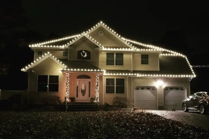 Festive home adorned with bright white Christmas lighting outlining the roofline and porch columns, creating a warm and inviting holiday ambiance.