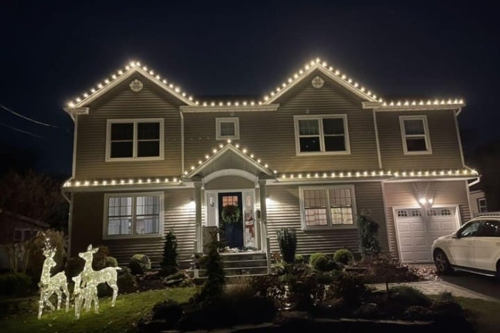 Home with Christmas lighting: A two-story home adorned with bright, warm white Christmas lights outlining the roofline, complemented by illuminated deer lawn decorations.