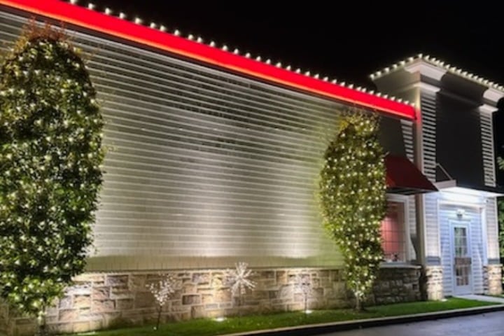 Commercial holiday lighting adorns a building's facade, with trees wrapped in lights, snowflakes on the stone base, and a red-lit awning for a festive, inviting look.