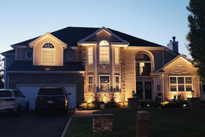 Elegant two-story home illuminated with outdoor lighting. The exterior features a mix of siding and stone, with a dark roof and well-manicured lawn. Perfect for showcasing Christmas lighting ideas.
