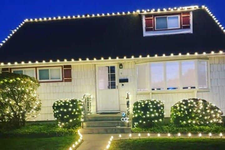 House decorated with Christmas lighting, including roofline, bushes, and walkway lights. Festive and bright, this is classic Christmas lighting.