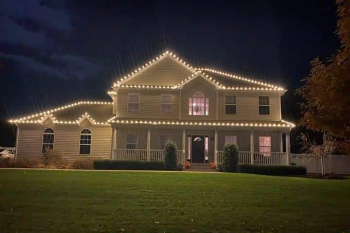 Large home illuminated with warm white Christmas lighting along the roofline. The dark sky provides a stark contrast, highlighting the holiday cheer.